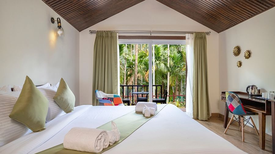 A view of our cottages with a large bed, furniture and a view of the garden seen from the inside - Stone Wood Nature Resort, Gokarna