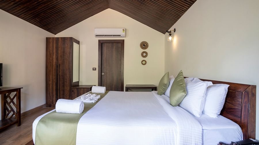 A hotel room with a large bed with a green runner, plush pillows and a large wooden cupboard by the side - Stone Wood Nature Resort, Gokarna