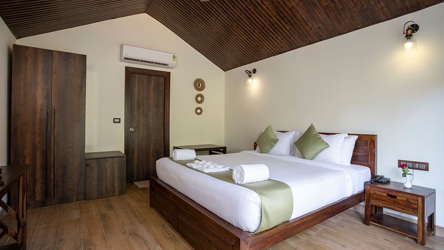 Another angle of a a hotel room with a large bed with a green runner, plush pillows, a night desk and a large wooden cupboard by the side - Stone Wood Nature Resort, Gokarna