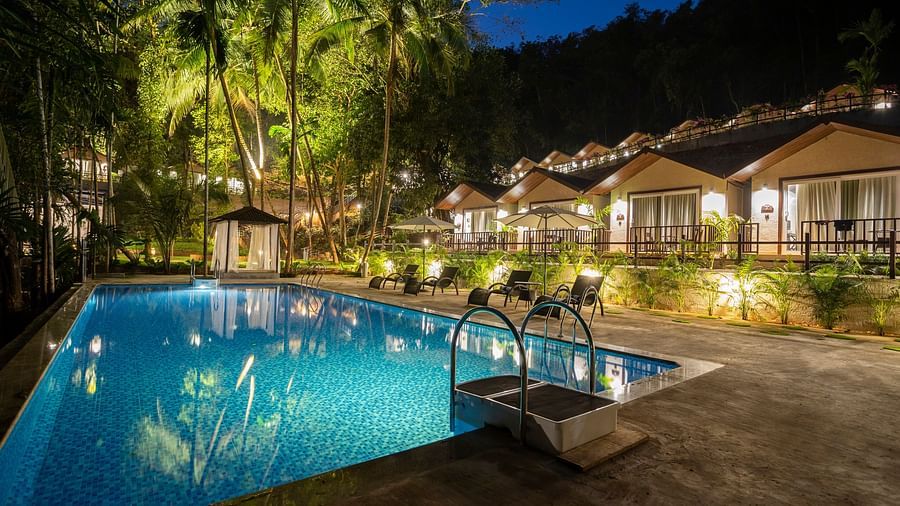 A night time view of the cottages by the pool illuminated by bright lights - Stone Wood Nature Resort, Gokarna