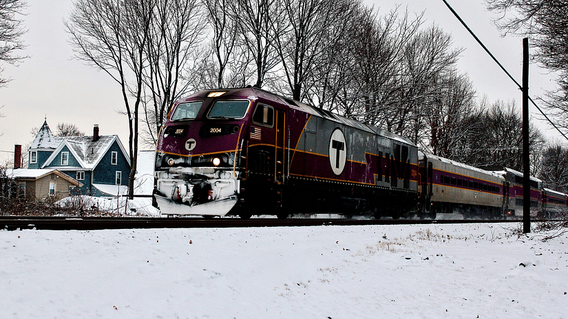 An overview of a train with snow covering around it and bare trees next to it