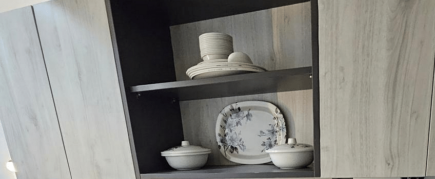 A low-angle view of the cupboard and a shelf with neatly arranged plates and cups at Urban Suites by BluSalzz, Jaipur.