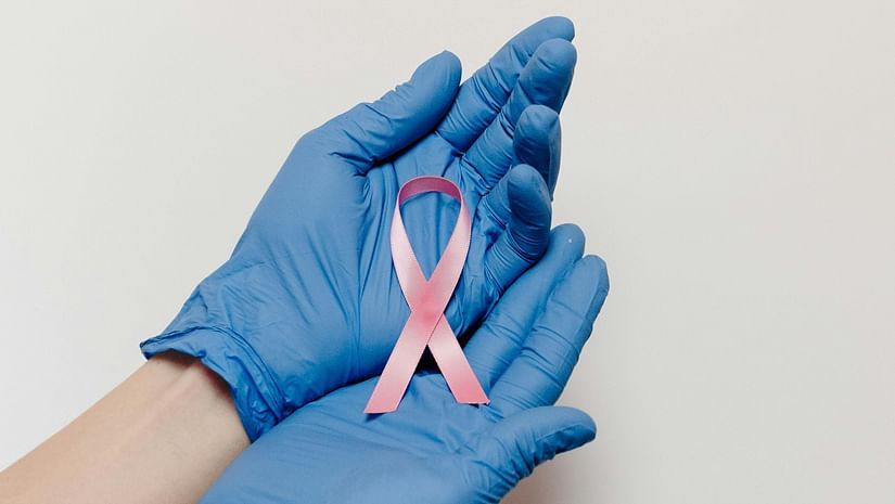 Two gloved hands gently hold a ribbon, folded to symbolise cancer.