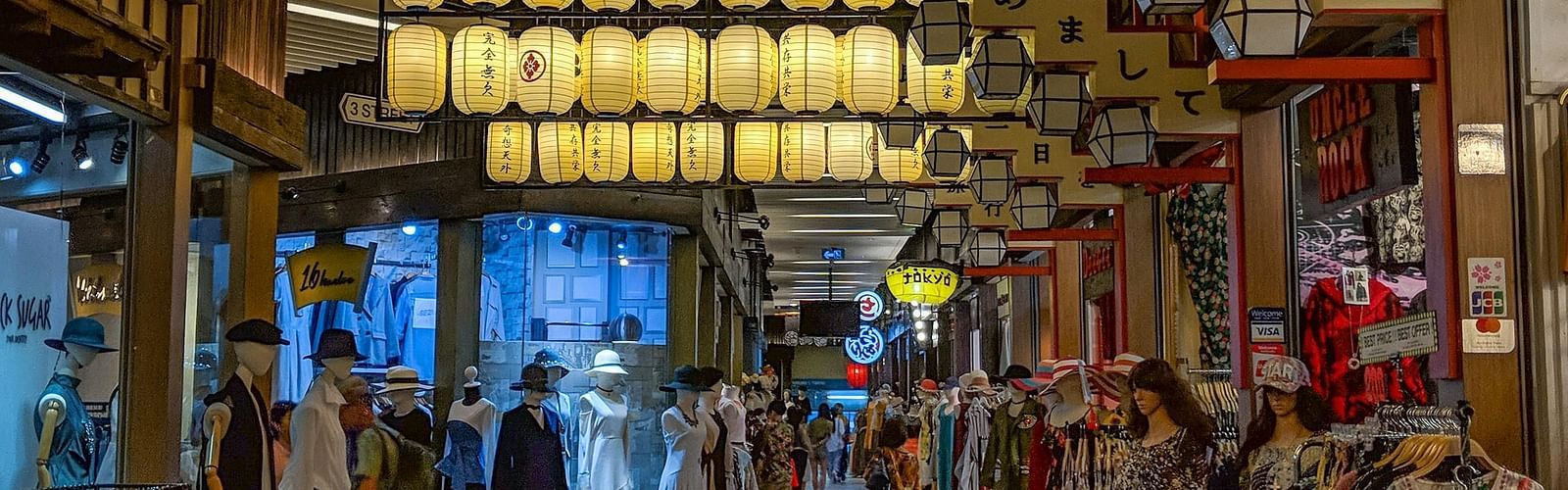 a crown walking inside a mall with clothes hanging outside from the shops inside a mall in Bangkok