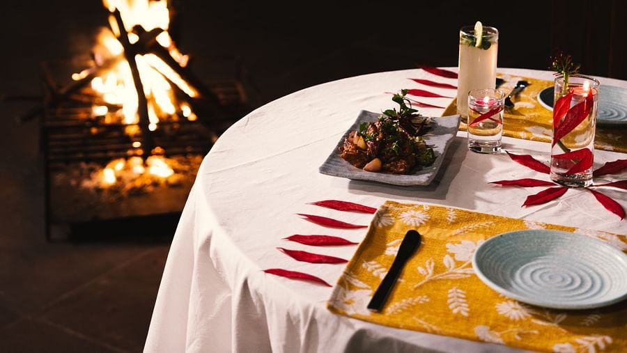 A beautifully set dinner table at BluSalzz Villas - The Green Roof, Bhimtal, with a warm campfire glowing in the background.