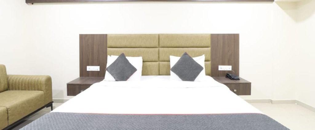 Front view of the double bed with a grey-coloured bed runner spread over it in the Premium Room of Pravasa Stay, Ahmedabad (Alba Premier).