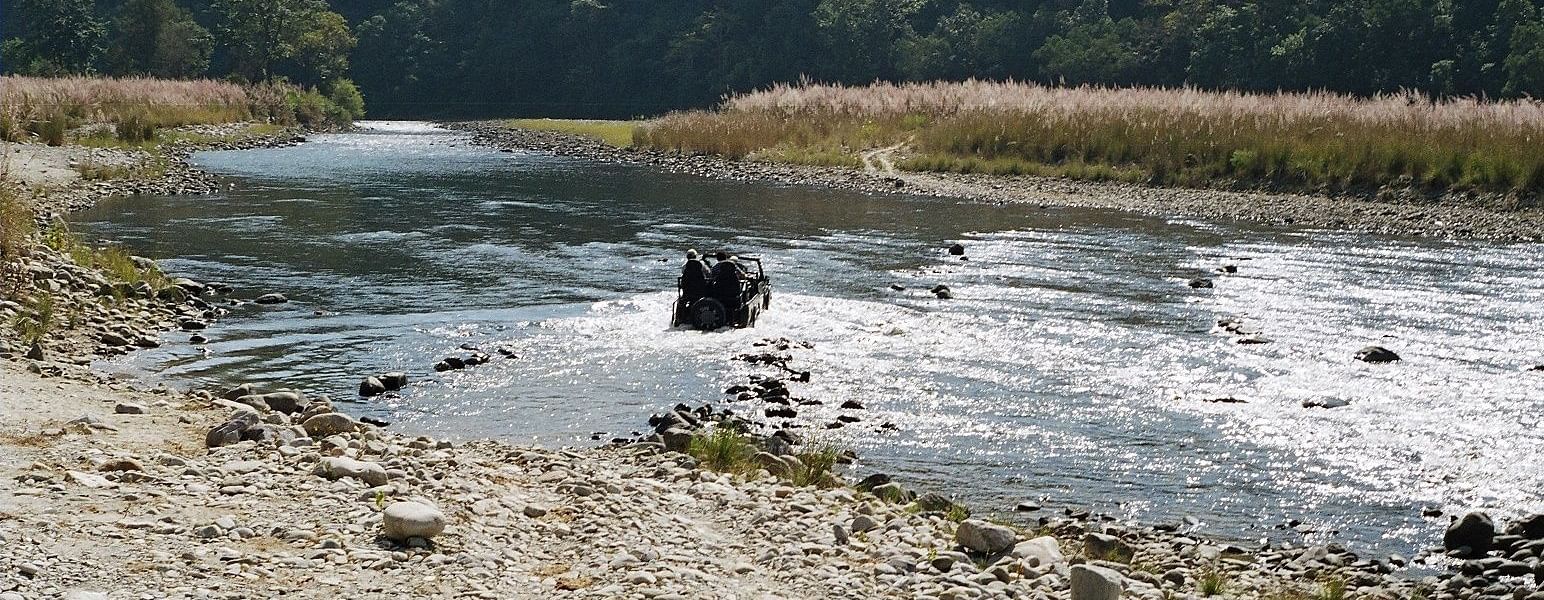 An image featuring a river crossing of people in a jeep and forest in the background.