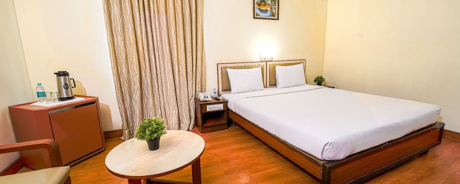 Bright hotel room with a double bed, wooden flooring, and a seating area by the window in Hyderabad near Ramoji Film City.