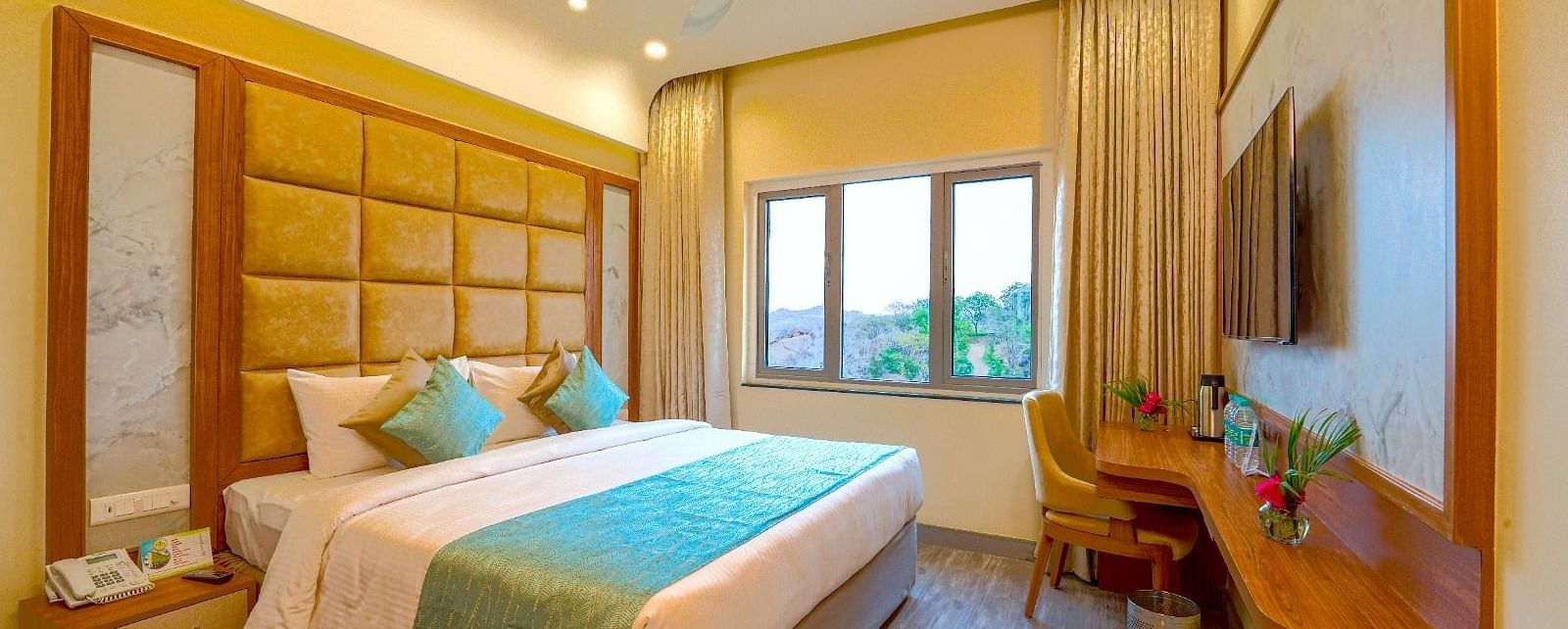 Cozy bedroom with a queen-sized bed, elegant headboard, and large window offering natural light at Tara, Comfort Hotel in Hyderabad - Ramoji Film City.