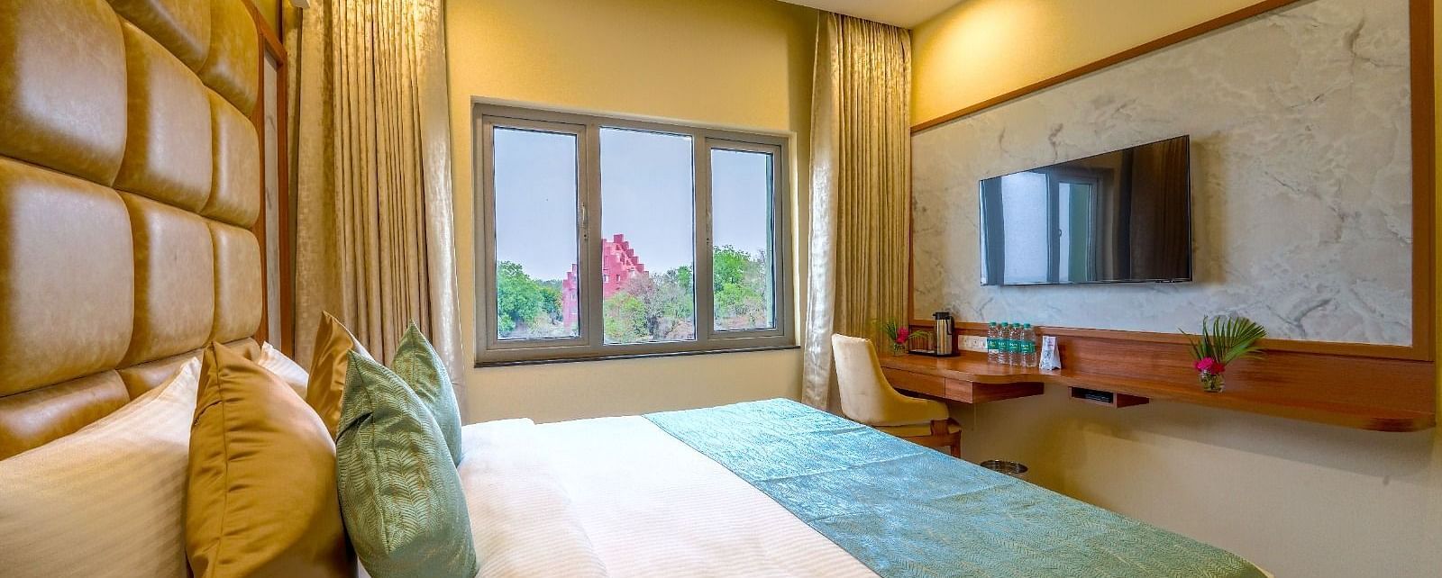 Bright and airy hotel room with a plush queen-sized bed, wooden accents, and a view of the greenery outside Tara, Comfort Hotel in Hyderabad - Ramoji Film City.