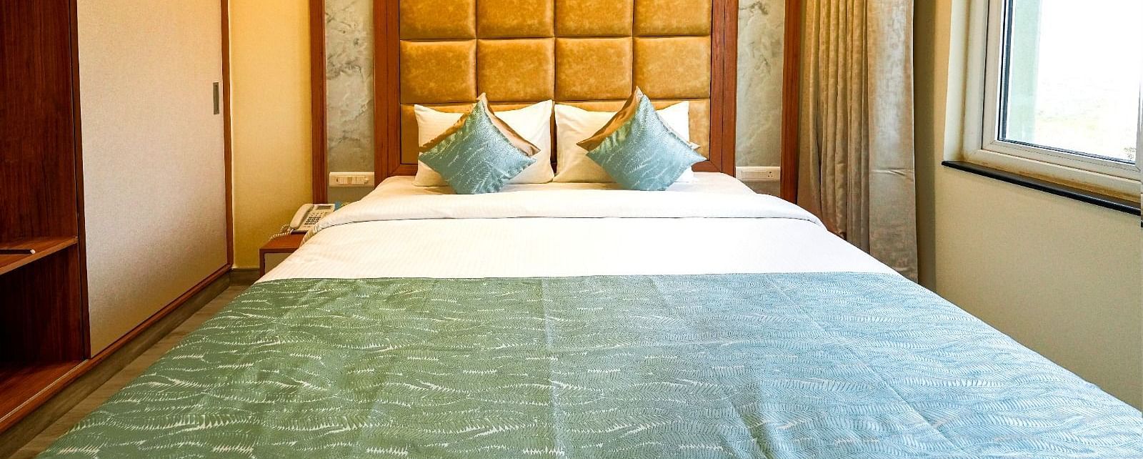 Inviting hotel room with a neatly made bed, cushioned headboard, and a view through the large window Tara, Comfort Hotel in Hyderabad - Ramoji Film City.