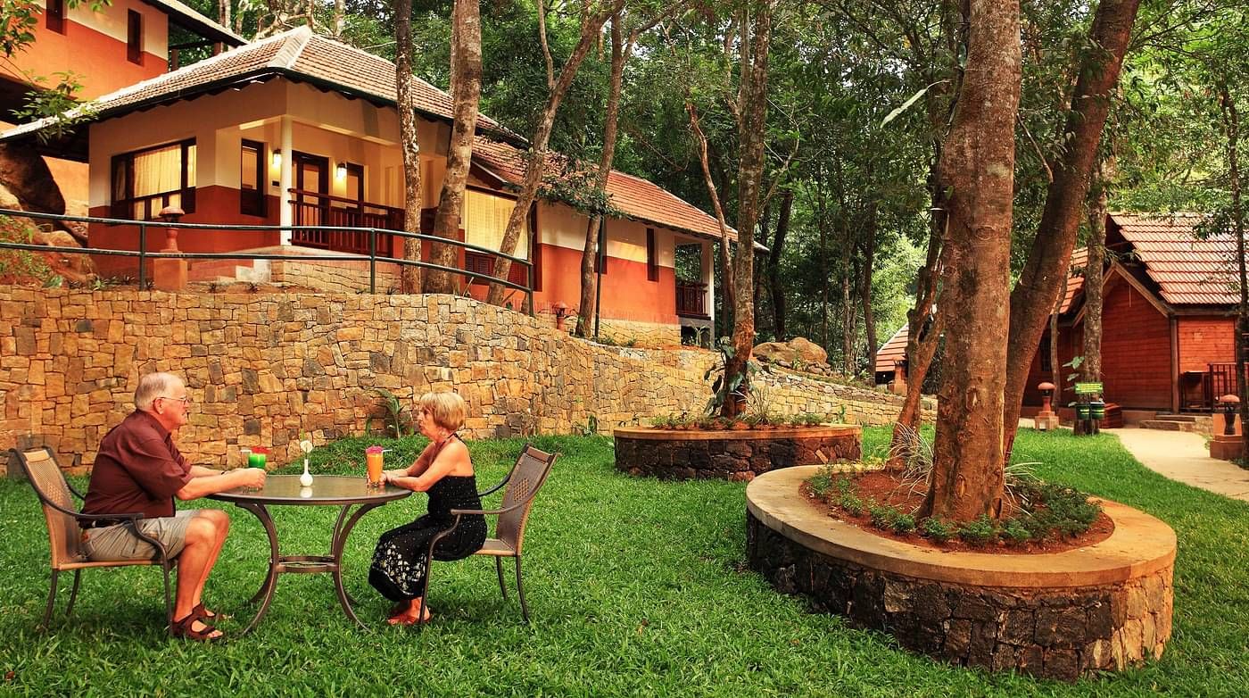 A couple sitting at a dining table outside villas amidst greenery | Vythiri Resort. Wayanad