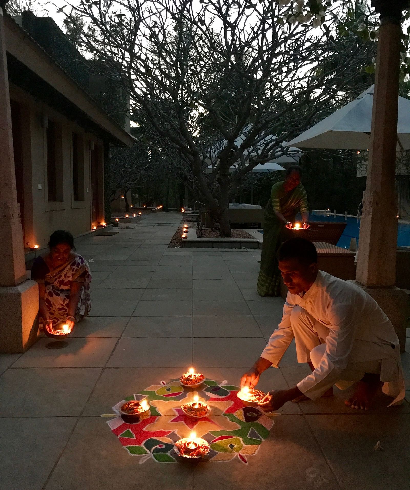 Person sitting on the ground with lit candles in bowls, outdoor setting, evening - Shreyas Retreat