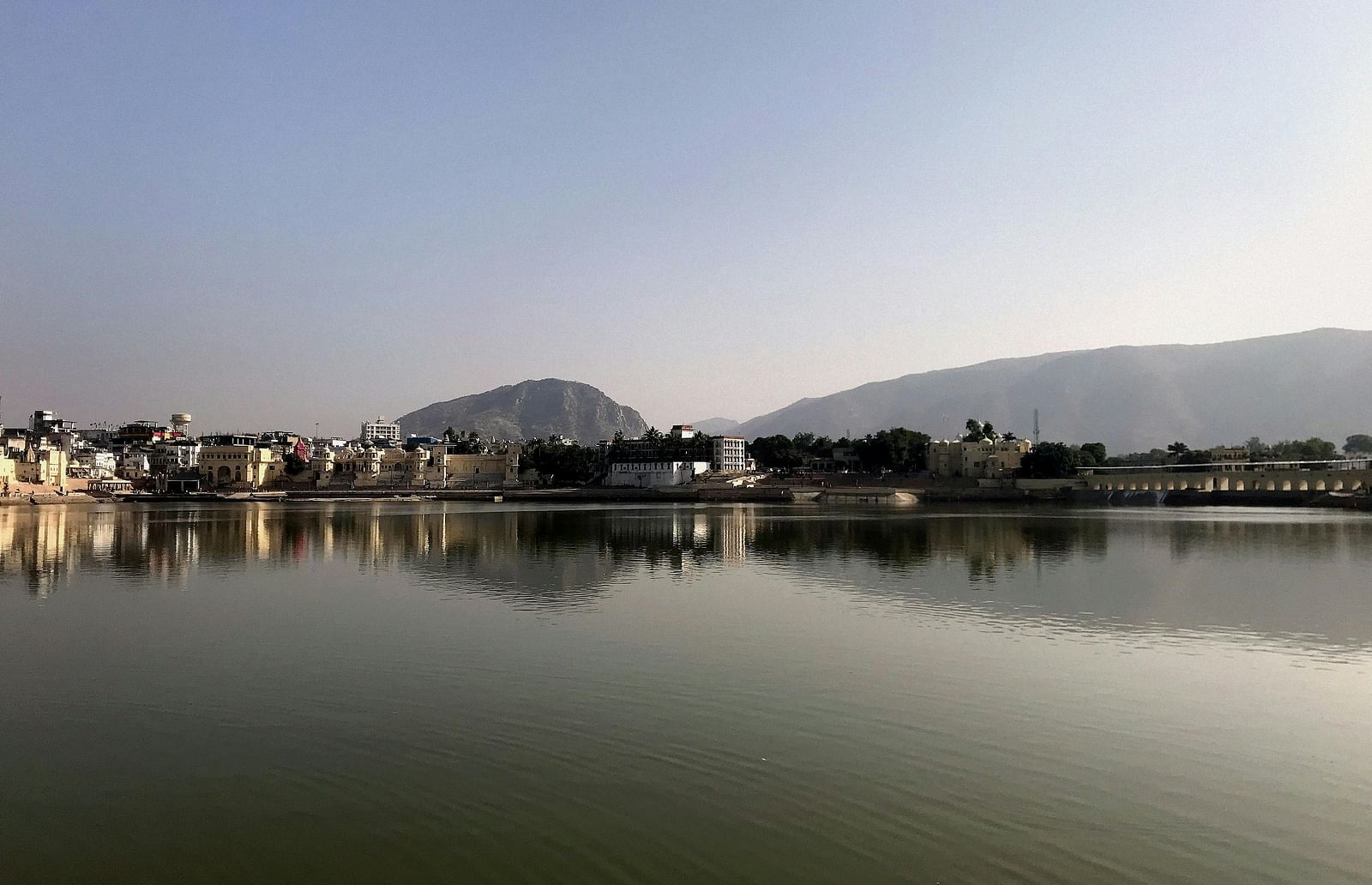 View of Lake Pichola with surrounding buildings and hills under a clear sky