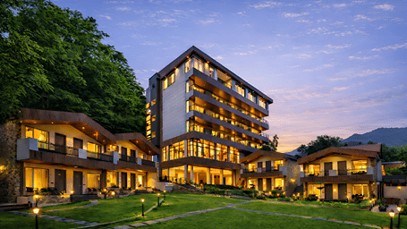 Twilight view of hotel complex and lawn area surrounded by forested hills at DLS Divine Resort & Spa, Manali.   