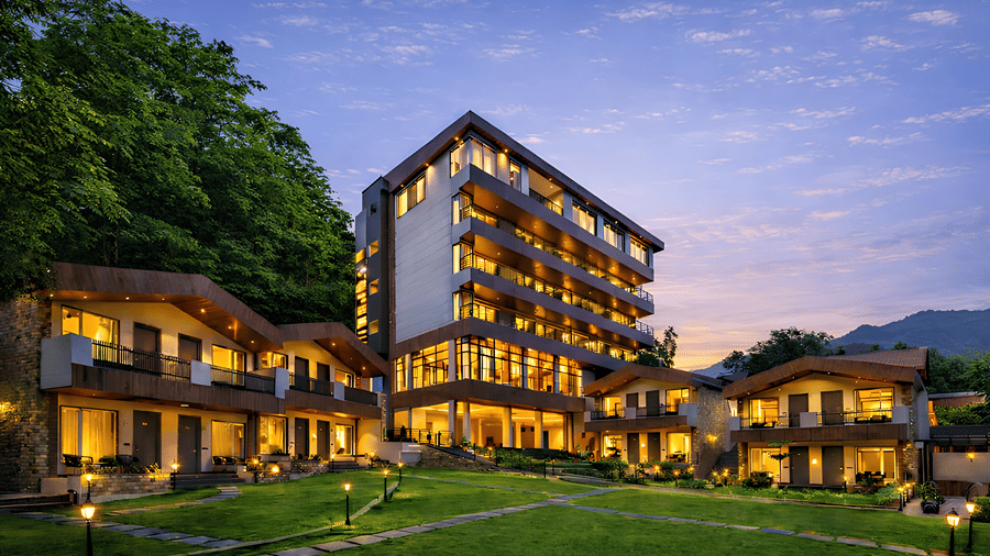 Twilight view of hotel complex and lawn area surrounded by forested hills at DLS Divine Resort & Spa, Manali.   