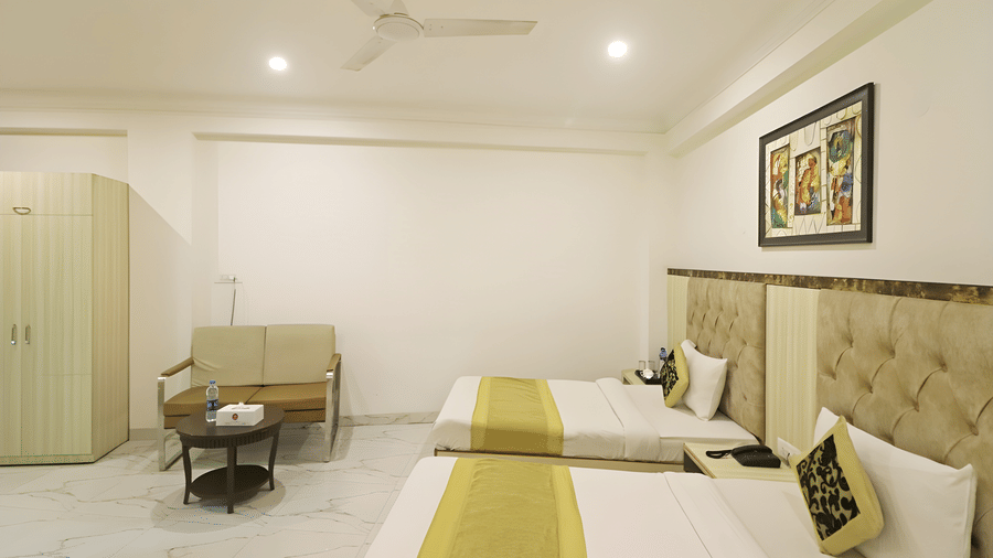 A guest room at Hotel Apple Park Delhi showing the twin beds next to a small seating area with a metal-framed sofa and a round coffee table.