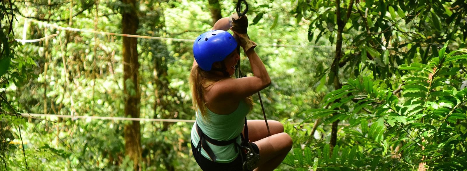 A person wearing a helmet and harness ziplining through a dense forest.