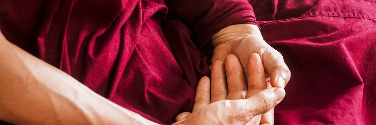 A serene moment of stillness captured in a close-up of meditative hands resting gently on maroon robes—symbolising mindfulness, inner peace, and the healing power of silence in spiritual wellness practices.