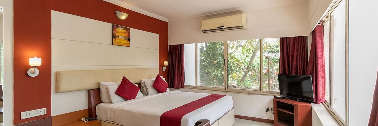 a double bed with side tables and lamps above the bed inside one of the rooms - VITS Presidency Daman