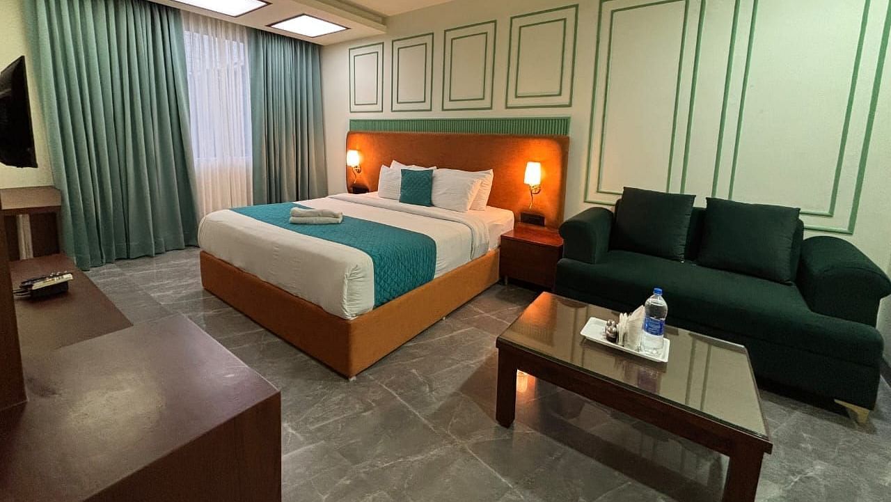 A spacious room with a double bed, a dark green sofa, and a wooden coffee table - Asian Suites IFFCO Metro, Gurgaon