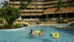 The Retreat Hotel and Convention Centre exterior view showing the large swimming pool with guests relaxing, surrounded by landscaped greenery and the hotel building in the background.