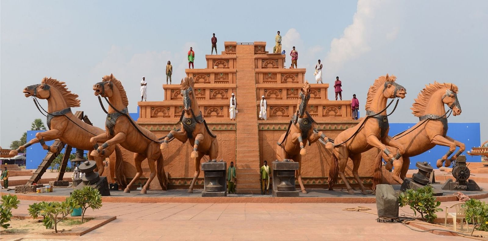 A large, dramatic sculpture display featuring multiple horses and a tiered castle structure, set in an outdoor park under a clear blue sky, showcasing artistic and cultural themes at Ramoji Film City Hotels in Hyderabad 