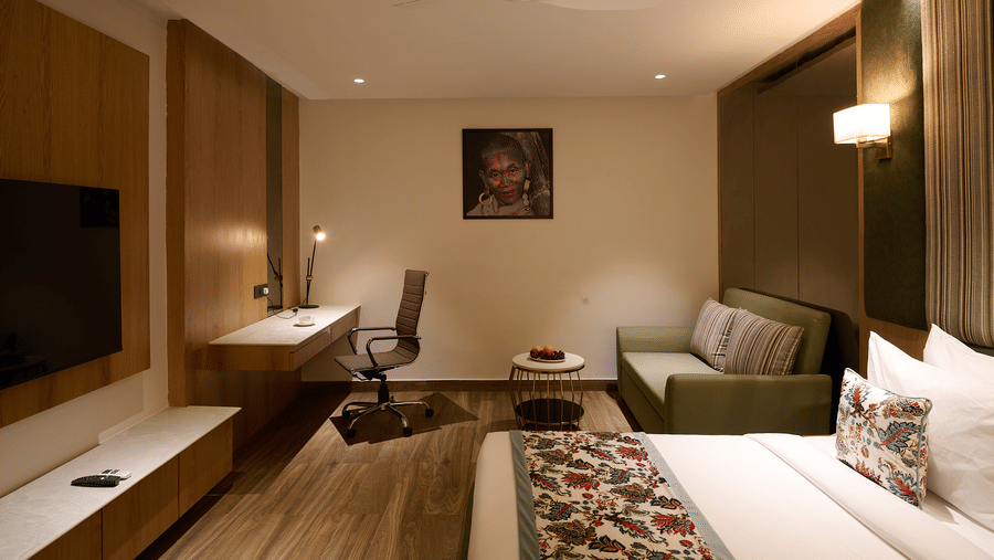 A hotel room with a double bed, a small sofa, a desk area with a chair, and a wall-mounted television | Voyage Eastin Suites