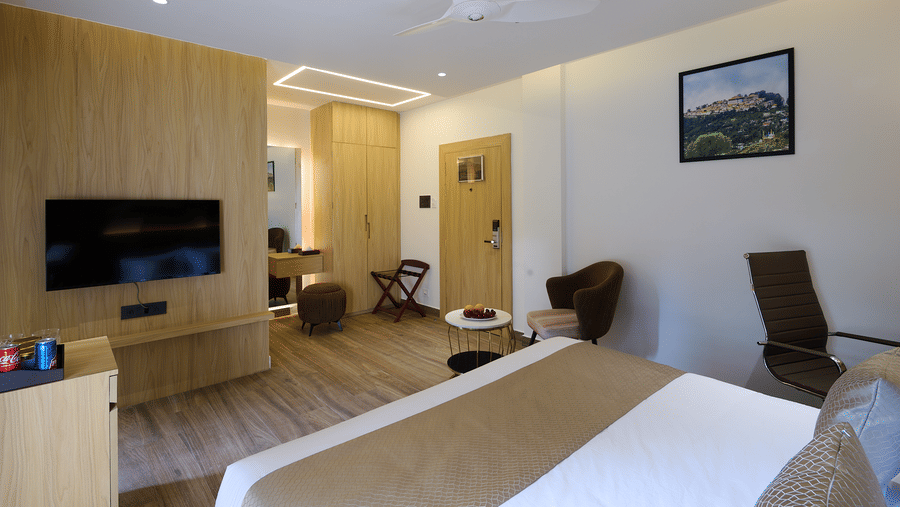 A wide shot of a hotel room with a double bed, light wood paneling, a wall-mounted TV, and an armchair in the corner | Voyage Eastin Suites