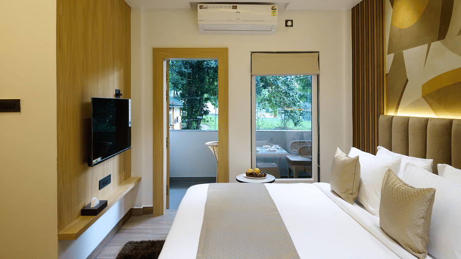 A hotel room with a double bed facing glass doors that open to outdoor views, a television, and a white ceiling with recessed lighting | Voyage Eastin Suites