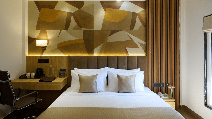 A brightly lit hotel room with a double bed, a geometric patterned accent wall behind the headboard, and a small desk area | Voyage Eastin Suites