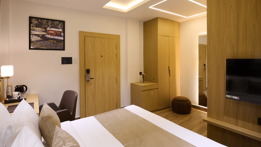 A hotel room with a double bed, a wooden wardrobe/storage area, a wall-mounted television, and a door leading to the outside or another area | Voyage Eastin Suites