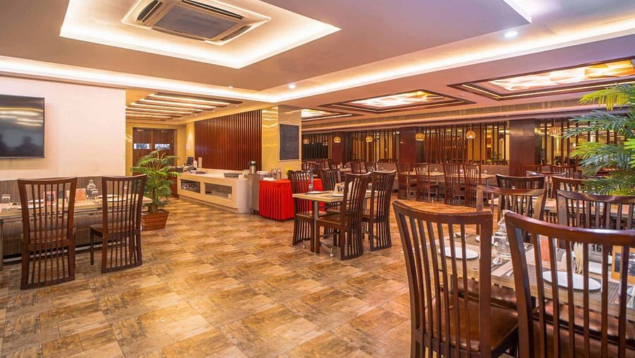 A wide shot of a spacious dining area with wooden tables and chairs, illuminated by warm ceiling lights at Mansha Hotel Regency.