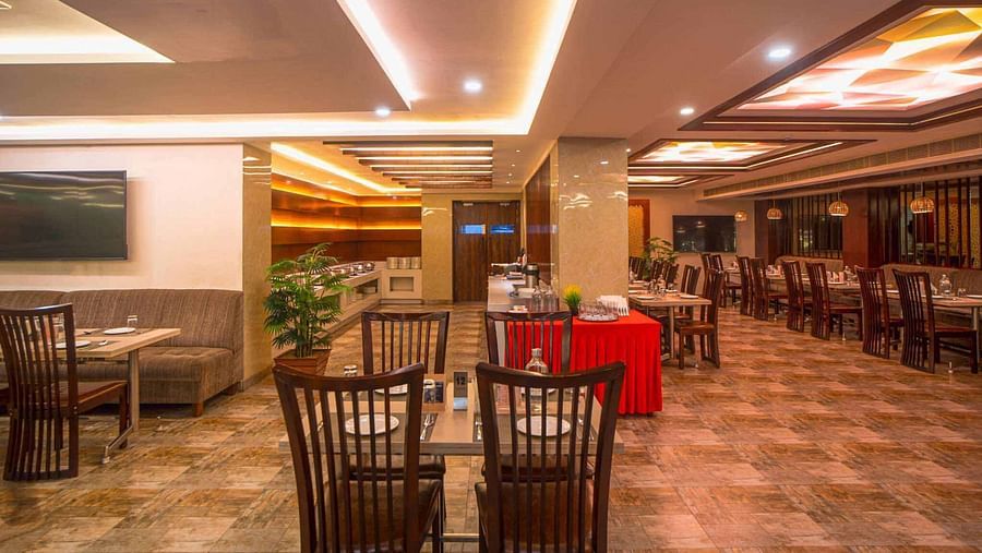 A modern dining room at Mansha Hotel Regency with warm lighting, wooden tables and chairs, and a television screen on the wall.