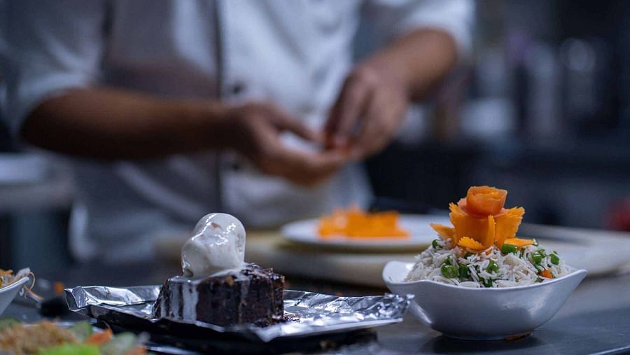 A blurred close-up shot of a chef's hands preparing dishes, with other plated items nearby - Mansha Hotel Regency