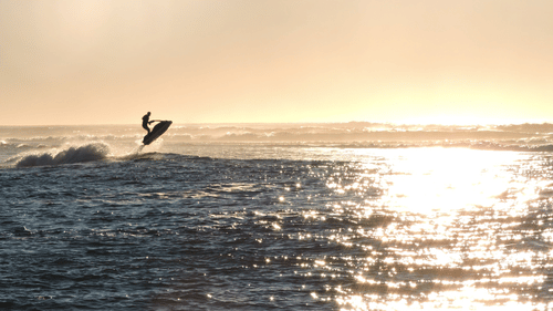 An overview of a person jumping over a large wave in the ocean with a Jetski.