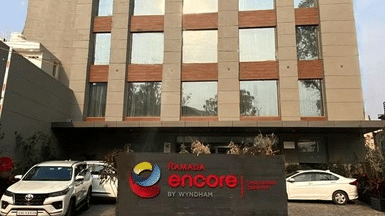 Front exterior view of the Ramada Encore by Wyndham Chandigarh Zirakpur hotel building with the main entrance and vehicles parked outside.