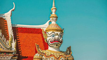 A view of a statues at Wat Arun, Bangkok, having large tooth protruding out of the mouth, armour and a headgear with a face on it.
