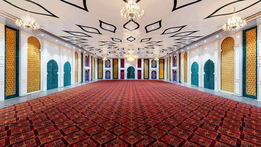Grand event hall with red patterned carpet, arched doorways, ornate ceiling lights, and golden-accented interior decor.