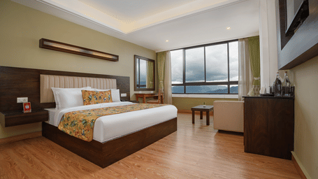 Deluxe Valley View Room at Summit North Star, Gangtok featuring a bed, work desk with chair, sofa chair and table, a cabinet table with tea and coffee maker, and a large window.