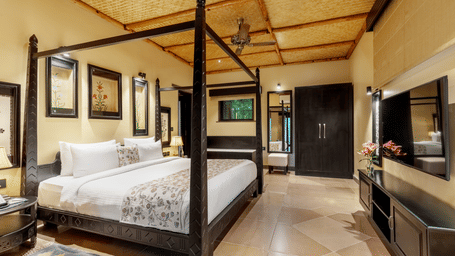 A refined guest room at Aamaghati Wildlife Resort showcasing a four-poster bed, warm lighting, stylish decor, and ample space with a wardrobe and modern comforts.