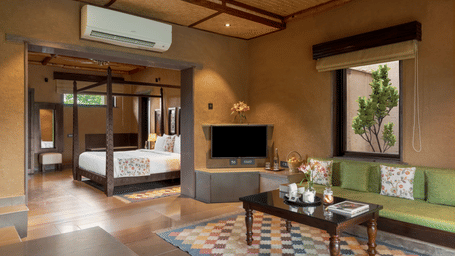 A premium room at Aamaghati Wildlife Resort featuring a cosy seating area, flat-screen TV, patterned flooring, and large windows creating a homely retreat.