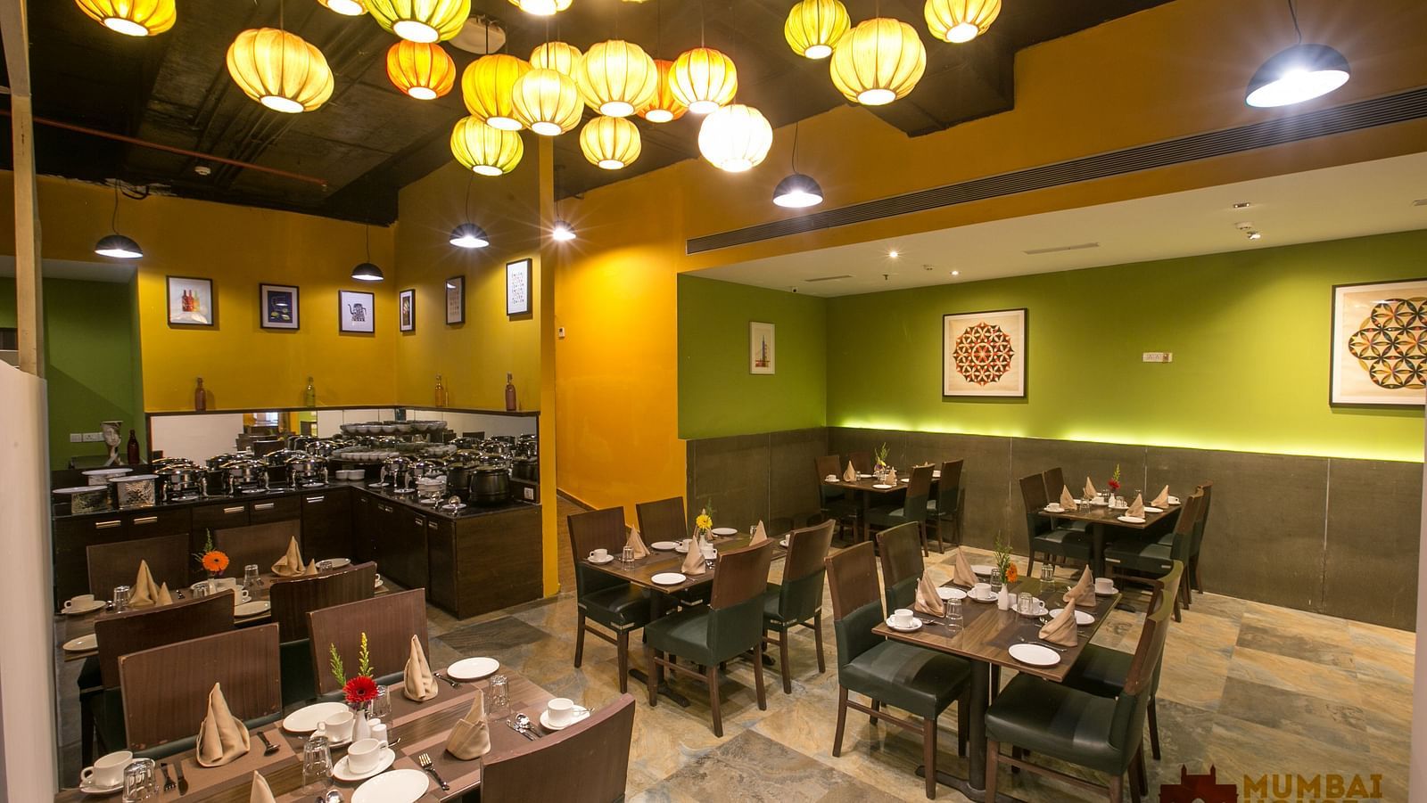 Hotel restaurant with colorful hanging lamps, art-decorated walls, wooden tables, and buffet area.