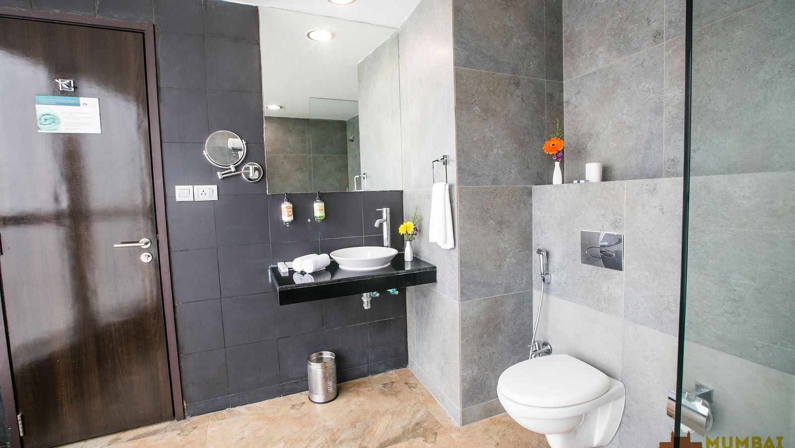 Contemporary bathroom featuring a toilet, a mirror, a sink with amenities, and grey tiled walls.