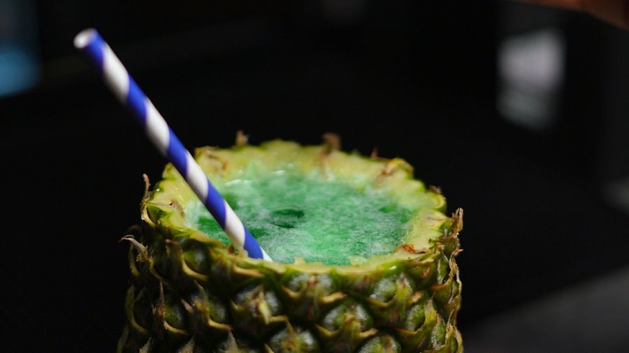 A hand preparing a pineapple drink with a straw, close-up shot at Cenneys Gateway.