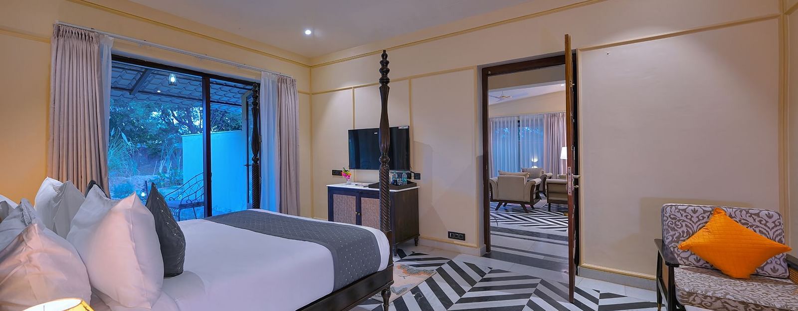 Luxury Suite Cottage with a four-poster bed, black and white chevron flooring, a seating area with an orange pillow, and a view into a living area - Singhvilas, Ranthambore