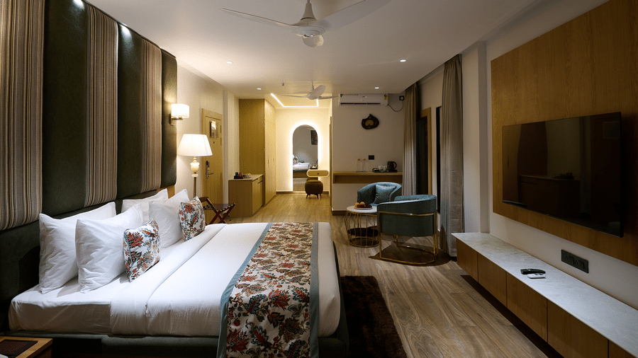 A spacious hotel suite with a double bed, a separate sitting area with sofas, a television, and an arched entryway in the background | Voyage Eastin Suites