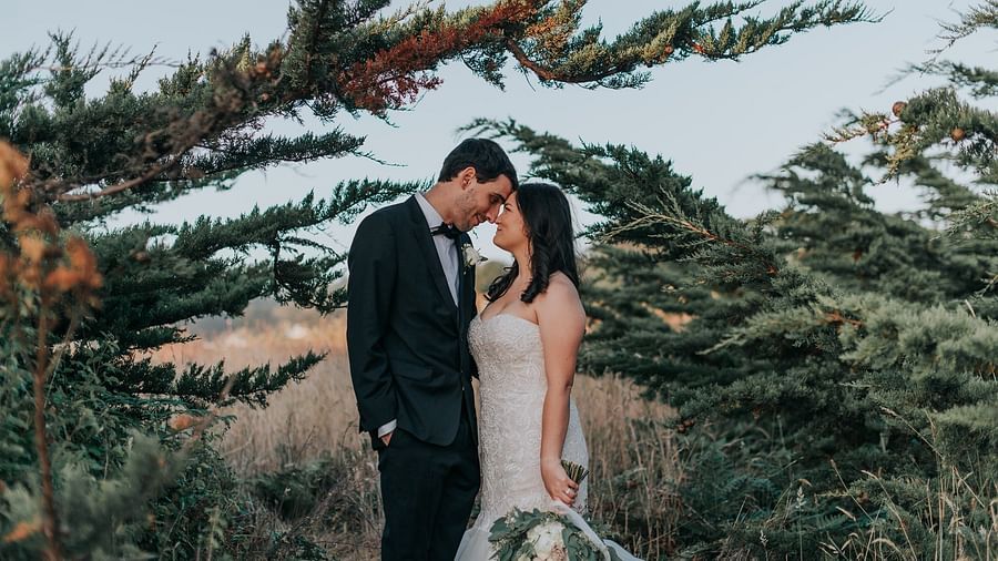 Bride and groom sharing a kiss, framed by lush greenery