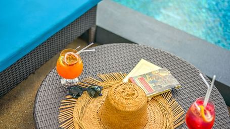 A table on the poolside with refreshing drinks, a straw hat, sunglasses and a book - Maikhao Dream Villa Resort & Spa, Phuket