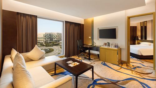 Image of at Premium Luxury Suite at Pride Plaza Hotel, New Delhi featuring the living room where a sofa set is placed in front of a TV along with a coffee table and the bedroom is seen from a corner